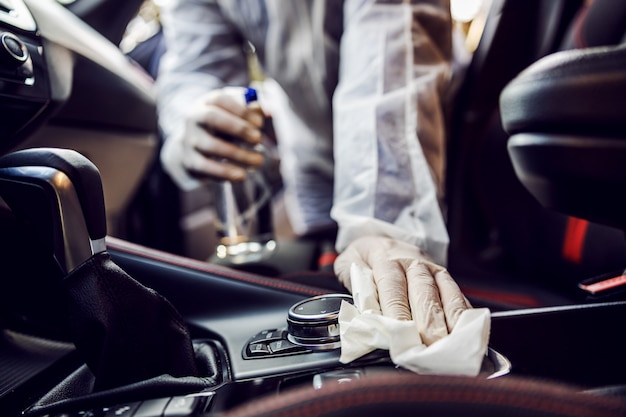 Zdjęcie mężczyzna w kombinezonie ochronnym z maską dezynfekującą wnętrze samochodu, wyciera czyste powierzchnie, które są często dotykane, zapobiega zakażeniu koronawirusem, zakażeniu zarazkami czy bakteriami. infekcja