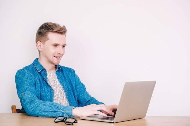 Mężczyzna w koszuli i okularach pracujący na laptopie siedzący na stole na białym tle