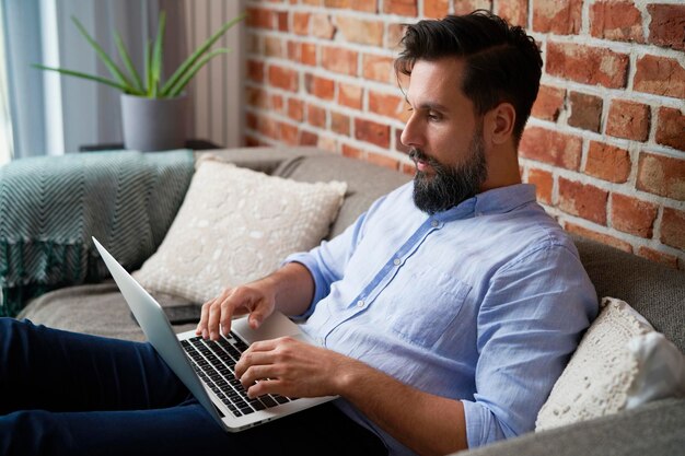 Mężczyzna w koszuli siedzący na kanapie i używający laptopa