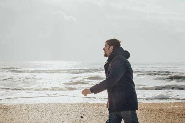 Mężczyzna w kurtce spaceruje brzegiem morza w zimowy dzień Podróże i piesze wycieczki