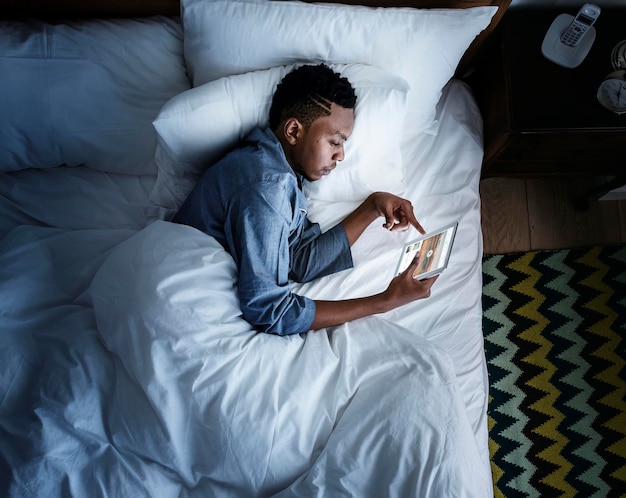 Mężczyzna w łóżku korzystający z urządzenia cyfrowego w ciemności