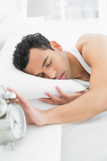 Mężczyzna w łóżku przedłużyć rękę budzik