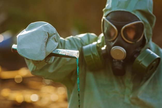 Mężczyzna w masce gazowej i zielonym wojskowym stroju bada beczki po katastrofie chemicznej