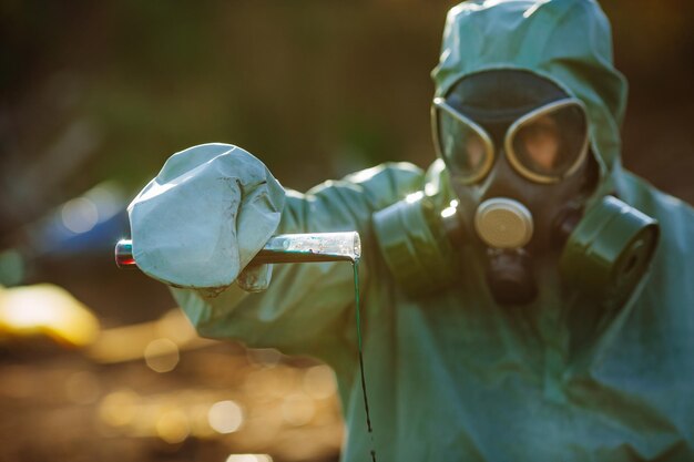 Zdjęcie mężczyzna w masce gazowej i zielonym wojskowym stroju bada beczki po katastrofie chemicznej