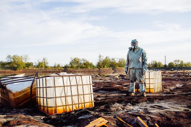 Mężczyzna w masce gazowej i zielonym wojskowym stroju bada beczki po katastrofie chemicznej