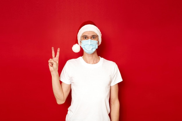 mężczyzna w masce medycznej Kapelusz Świętego Mikołaja pokazuje dwa palce z ręką znaku zwycięstwa pokoju w kształcie litery V