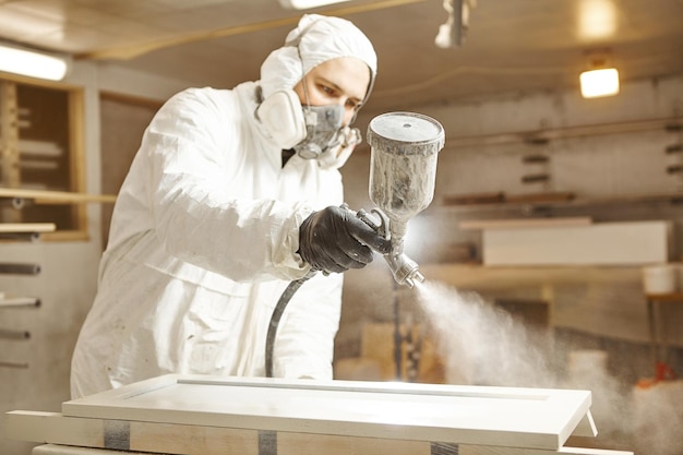 Mężczyzna w masce ochronnej malujący drewniane deski w warsztacie Zastosowanie środka zmniejszającego palność zapewniającego ochronę przeciwpożarową urządzenia do natrysku bezpowietrznego
