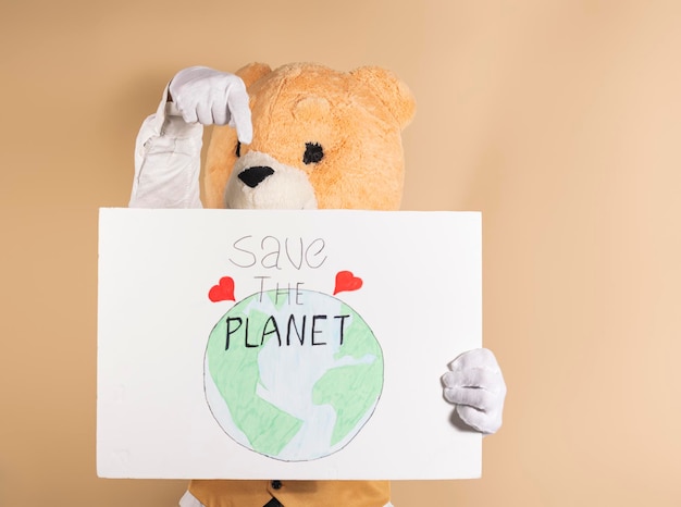 Mężczyzna w masce pluszowego misia na żółtym tle wskazuje kartonowy znak z napisem 39 Ratuj planetę 39 Koncepcja dbania o planetę i globalne ocieplenie