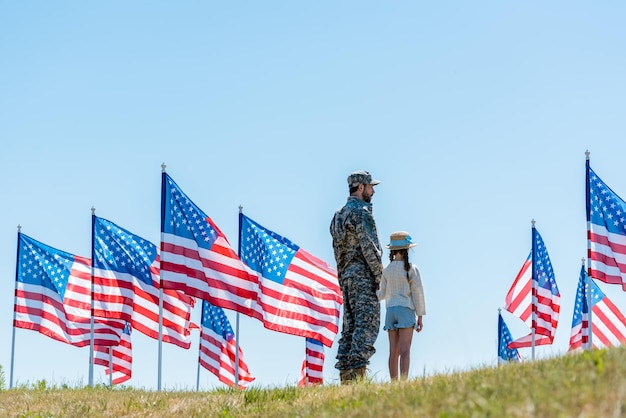 Zdjęcie mężczyzna w mundurze wojskowym stojący z córką w pobliżu amerykańskich flag