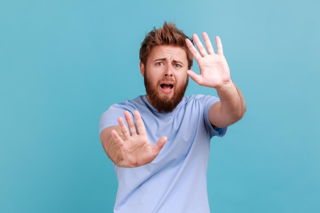 Mężczyzna w niebieskiej koszulce krzyczy z przerażenia i strachu trzyma ręce w górze, by bronić się przed atakiem paniki