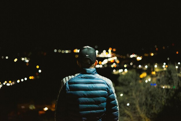 Mężczyzna w niebieskiej kurtce patrzy na nocne światła miasta.