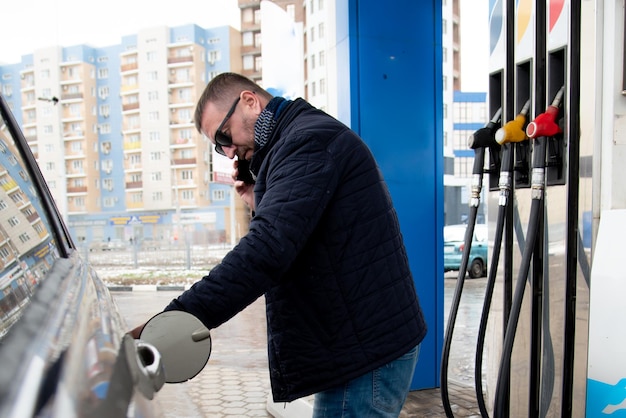 Mężczyzna w niebieskiej marynarce i ciemnych okularach na stacji benzynowej Tankuje samochód Petrol Lifestile