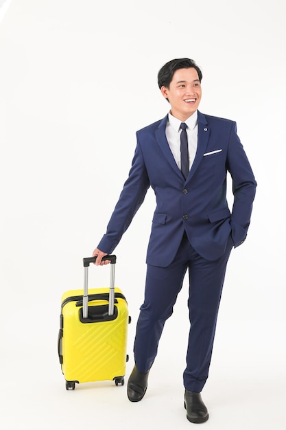 Mężczyzna w niebieskim garniturze trzyma żółtą walizkę i stoi z ręką na rączce.