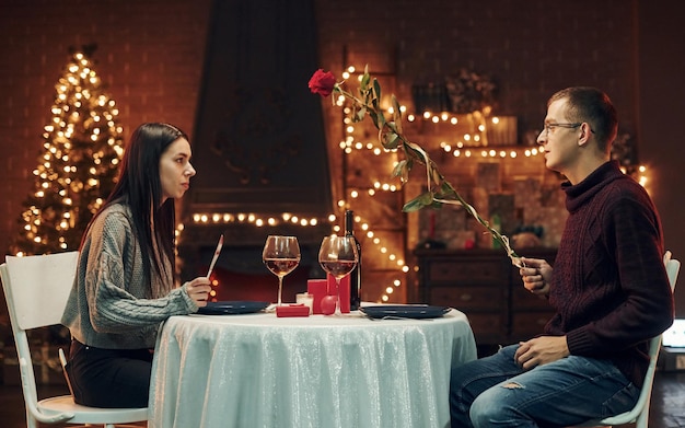 Mężczyzna w okularach i młoda brunetka siedzi przy stole w pomieszczeniu Romantyczna kolacja