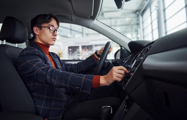 Mężczyzna w okularach i ubraniach formalnych siedzi wewnątrz nowoczesnego samochodu.