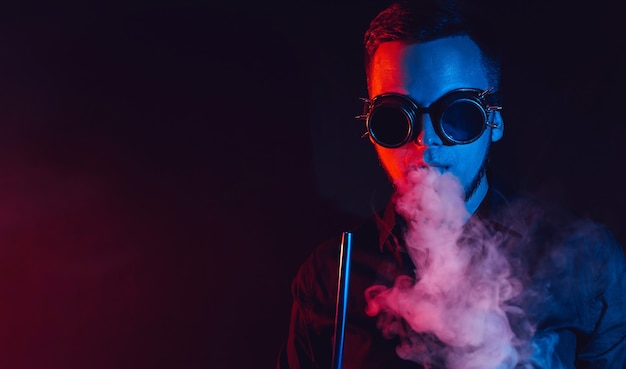 mężczyzna w okularach pali fajkę wodną i wydmuchuje chmurę dymu
