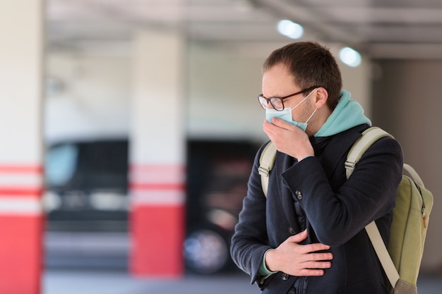 Mężczyzna w okularach źle się czuje podczas parkowania, kaszlu, w masce ochronnej przed przenośnymi chorobami zakaźnymi i koronawirusem