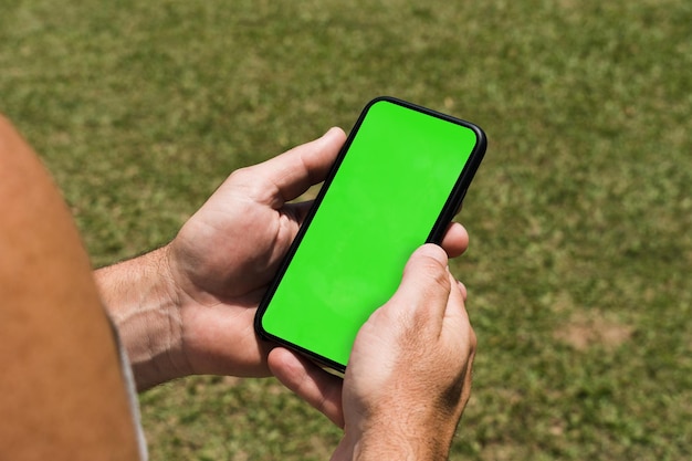 Mężczyzna w parku trzymający smartfona z aplikacją green screen na ekranie Rustykalny drewniany stół Chroma Key