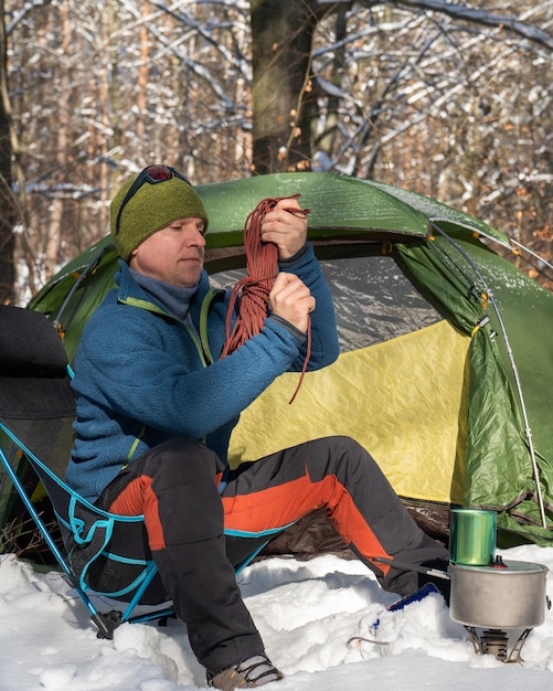 Mężczyzna w pobliżu namiotu przygotowuje się do jedzenia Zwija linę Noc w zimowym lesie Miłość do natury Ekoturystyka Słońce las śnieg Aktywny tryb życia Namiot na śniegu
