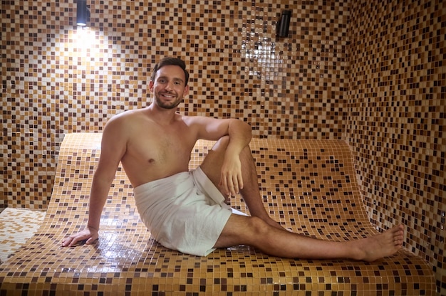 Mężczyzna w ręczniku siedzący w saunie i mający sesję detoksykacyjną
