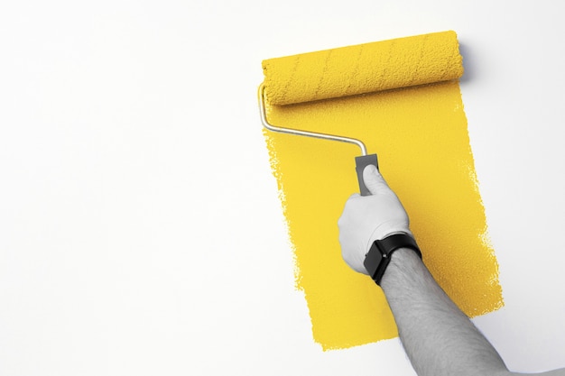 Mężczyzna w rękawiczkach maluje ręcznie ścianę na rozświetlający żółty kolor