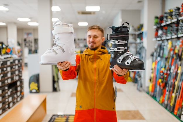 Mężczyzna W Sklepie Sportowym Pokazuje Biało-czarne Buty Narciarskie Lub Snowboardowe. Sezon Zimowy Ekstremalny Styl życia, Aktywny Wypoczynek, Klient Płci Męskiej Z Wyposażeniem Ochronnym