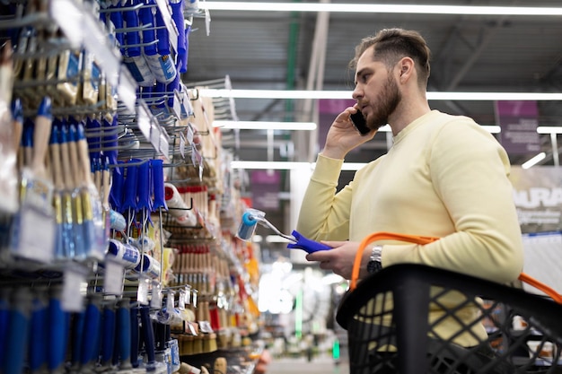 Mężczyzna w sklepie z narzędziami wybiera pędzle, rozmawiając o tym przez telefon z żoną