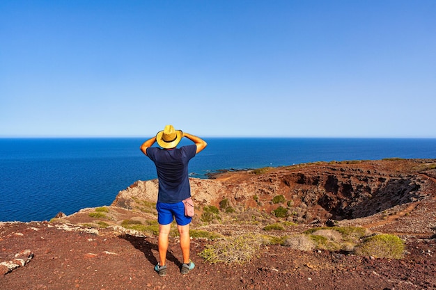 Mężczyzna w słomkowym kapeluszu spoglądający na morze ze szczytu wulkanu Monte Nero Linosa