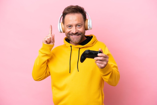 Mężczyzna w średnim wieku bawiący się kontrolerem gier wideo na różowym tle wskazujący świetny pomysł