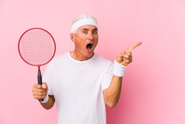 Mężczyzna w średnim wieku gry w badmintona na białym tle, wskazując z boku