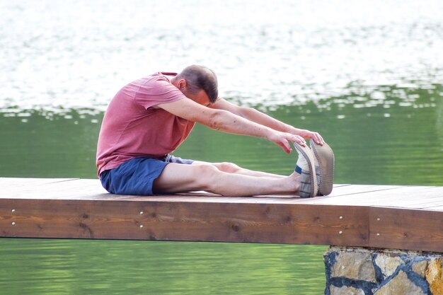 mężczyzna w średnim wieku robi asany jogi. Sportowiec trenuje na molo w letnim parku.