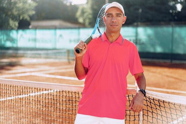 Mężczyzna w średnim wieku tenisista z rakietą, stojąc na korcie tenisowym w pobliżu netto