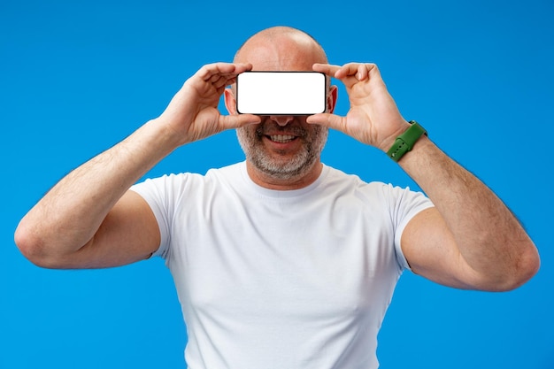Mężczyzna w średnim wieku trzymający pusty smartfon na oczach w studiu