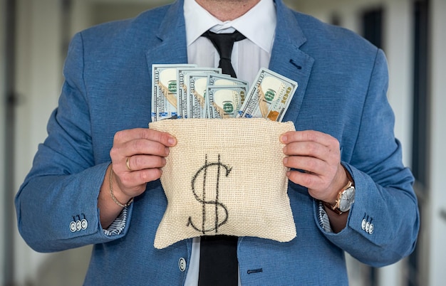 Mężczyzna w średnim wieku w biznesowej koszuli trzyma torbę dolarów ze złą twarzą Pojęcie pieniędzy, których nie chcesz dać