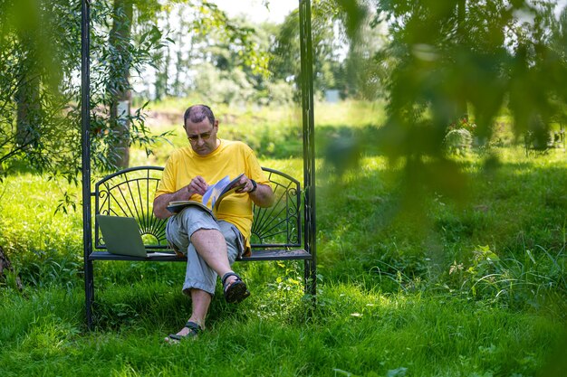 Mężczyzna w średnim wieku z laptopem i dokumentami pracującymi na zewnątrz w koncepcji ogrodu zielonego domowego biura