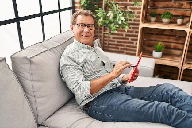 Mężczyzna w średnim wieku za pomocą touchpada siedzi na kanapie w domu