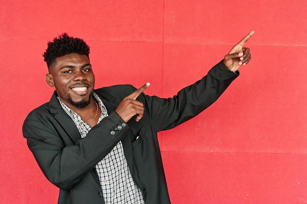 Mężczyzna w swobodnym blezerze wskazuje, aby skopiować przestrzeń na czerwonym tle, uśmiechnięty młody mężczyzna z Afryki