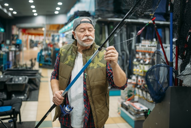 Mężczyzna wędkarz zakłada żyłkę w ucho wędki w sklepie wędkarskim.