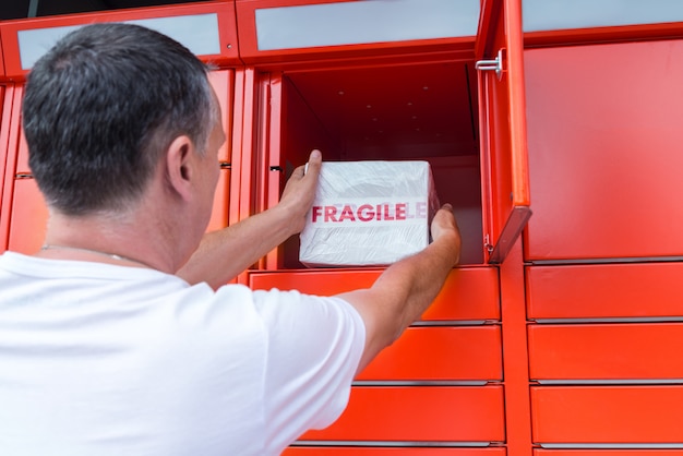 Mężczyzna wkłada pudełko do samoobsługowej skrzynki pocztowej