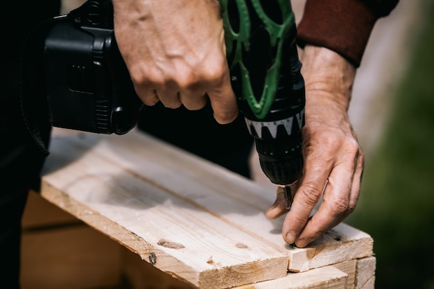 Mężczyzna wkręca śrubę w drewniane pudełko za pomocą śrubokręta bezprzewodowego Naprawa produktu za pomocą profesjonalnego elektrycznego śrubokręta Zbliżenie