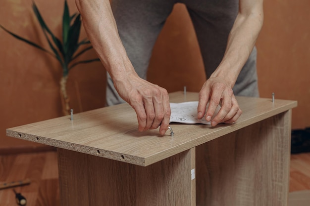 mężczyzna wkręca śrubę z metalowym kluczem imbusowym w drewnianą deskę podczas montażu nowego stołu