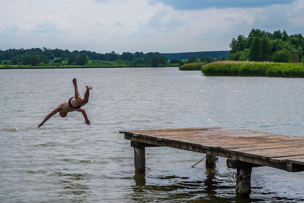 Mężczyzna wskakuje do wody jeziora w pobliżu drewnianego molo