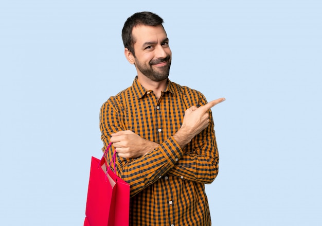 Mężczyzna wskazuje z boku z torba na zakupy przedstawiać produkt na odosobnionym błękitnym tle