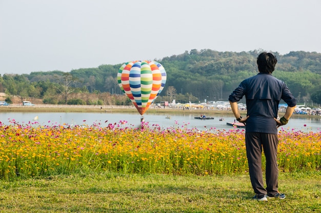 Mężczyzna wstał, odwrócił się, spojrzał na balon, unosząc się nad wodą z kwiatem kosmosu z przodu.