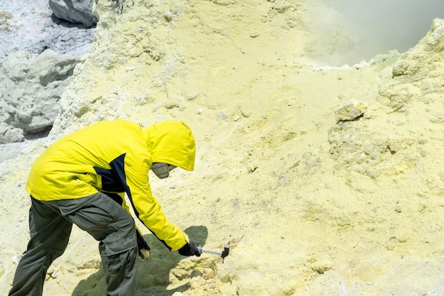 Mężczyzna wulkanolog na zboczu wulkanu obok dymiącego fumarolu pobiera próbkę minerału z krawędzi krateru siarki