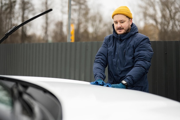 Mężczyzna wyciera maskę amerykańskiego samochodu SUV ściereczką z mikrofibry po umyciu w chłodne dni