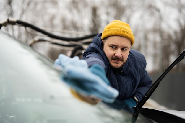 Mężczyzna wyciera przednią szybę amerykańskiego samochodu SUV ściereczką z mikrofibry po umyciu w chłodne dni