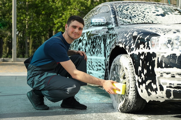 Mężczyzna wyciera samochód gąbką. Myjnia samochodowa. Jasna koncepcja samochodu