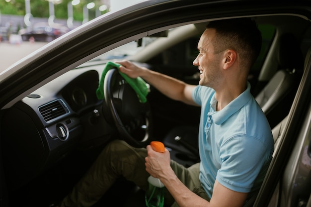 Mężczyzna wyciera wnętrze samochodu szmatą, ręcznie myje auto