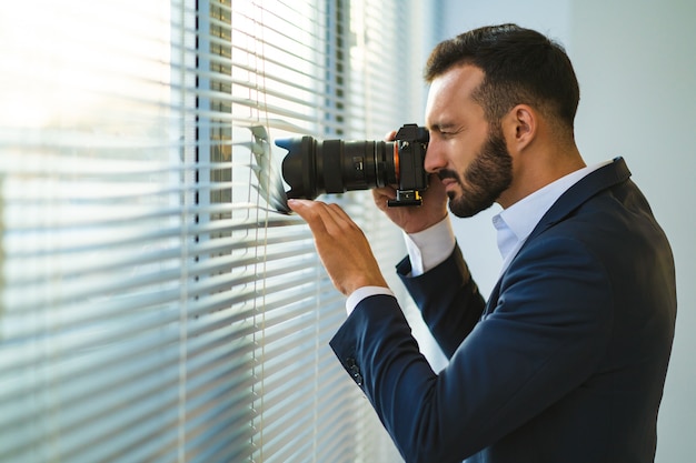 Mężczyzna z aparatem fotografujący przez żaluzje